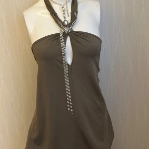 Halter neck top - Halter neck top with rhinestone strap around the neck. Never worn, but unfortunately the label got some spots on it (see picture). Original price: 659 kr. It says it fits all sizes, but it’s recommended for large and above.