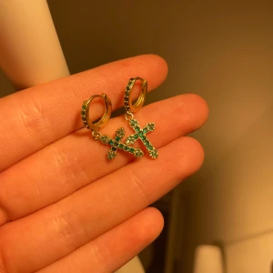 Guldörhängen med gröna kors - Snygga guldörhängen med hängande kors dekorerade med gröna stenar. Ringen och korsen är täckta av glittrande gröna detaljer som ger en cool och unik look. Perfekt för dig som vill sticka ut med dina smycken. Kan diskutera pris!! 💚