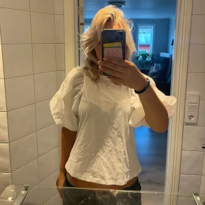 Vit blus med puffärmar från Love M - Säljer en vit blus från Love M i storlek M. Blusen har riktigt stora puffärmar och en rak, lite croppad passform. Tillverkad i bomull, perfekt för dig som vill ha en trendig och luftig topp med statement-ärmar.