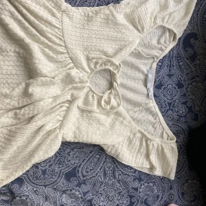 Vit kortarmad blus med knyt från 157 - Supersöt vit blus från 157 i storlek XS. Blusen har en lätt skrynklig struktur, korta ärmar och en snygg knytning framtill vid halsen. Perfekt för varma dagar och har en luftig, avslappnad passform.