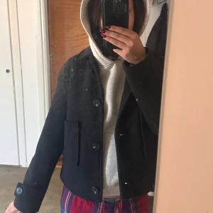 Svart ulljacka från 157, XS - Säljer en svart, kort ulljacka från 157 i storlek XS. Jackan har klassisk krage, stora knappar framtill och två fickor. Perfekt för dig som gillar en clean och stilren look med lite boxig passform.