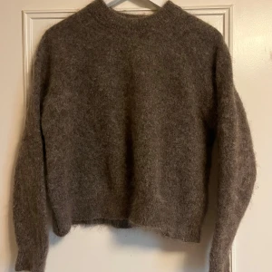 Brun stickad tröja i mohair från Zara Knit - Supermjuk och fluffig brun stickad tröja från Zara. Tröjan har en enkel, rak passform med rund hals och långa ärmar. Tillverkad i en mohairblandning med 70% mohair som ger en lyxig och mysig känsla. Perfekt för lager-på-lager under kyliga dagar. Storlek S, längd 50cm och bredd från armhåla till armhåla 49cm. 