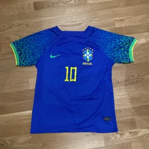 Blå Brasilien fotbollströja 2022 Nike - Snygg blå Brasilien fotbollströja från Nike med nummer 10 på bröstet och CBF-emblem. Ärmarna har leopardmönster i blått och grönt med gula detaljer vid mudden. Tillverkad i lätt och ventilerande polyester, perfekt för match eller träning. Strolek M men passar även S.