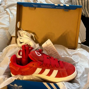 Röda Adidas Campus sneakers mocka - Säljer ett par röda Adidas Campus sneakers i mocka med klassiska vita ränder och vit sula. Skorna har snörning och kommer med extra vita skosnören. Perfekta för dig som vill sticka ut med färg. Det är storlek 37 1/3 och aldrig använda utan råkade köpa 1 par för mycket. 
