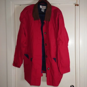 Röd parkajacka från Alberta - Röd parkajacka från Alberta med brun krage i mocka och blå detaljer vid fickorna. Jackan har knäppning med knappar framtill, långa ärmar och flera praktiska fickor. Perfekt för dig som vill sticka ut med färg och stil under höst och vinter.