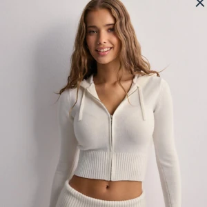 Vit kofta från Nelly - Superfin vit kofta från Nelly med dragkedja framtill och huva med snörning. Stickad känsla och bred ribbad mudd vid midjan. Perfekt för dig som gillar en trendig och bekväm look. Storlek S!