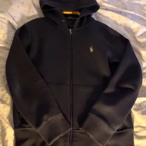 Svart hoodie från Polo Ralph Lauren XS - Svart hoodie från Polo Ralph Lauren i storlek XS. Klassisk design med dragkedja framtill, huva och det ikoniska broderade logot på bröstet. Mjuk och skön, perfekt för chill dagar. Snygg passform och ribbade muddar vid ärmslut och midja. Obs ett hål vid fickan bakom armen. Annars jätte fin 