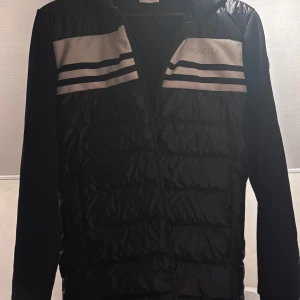 Svart Moncler pufferjacka med huva - Svart/blå pufferjacka från Moncler med huva och dragkedja. Köpt på NK i Sthlm Ny pris 10500(Kvitto finns) perfekt för hösten. Stilren o fräsch 