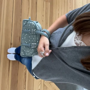 Handväska - En blå väska med strass detaljer, den är i denim material. Det finns även ett band till om man skulle vilja ha den hängandes på axeln💗