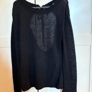 Svart stickad tröja med öppen rygg - Svart stickad tröja med långa armar och öppen rygg som knyts med band upptill. Ganska tunn men varm.