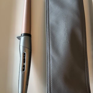 Remington PROluxe Curling Wand - Remington PROluxe Curling Wand med konformad stav för naturliga lockar. Digital display, justerbar temperatur och snabb uppvärmning. Säljs med original värmeskyddande fodral. Mycket fint skick, inga synliga defekter eller slitage.