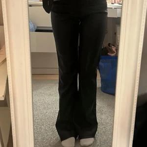 Svarta bootcut byxor i skinnimitation - Snygga svarta byxor i skinnimitation från g perfect jeans, modell med bootcut och normal passform. Byxorna har klassiska fickor, bälteshällor och dragkedja framtill. Perfekta för dig som vill ha en edgy look med lite glansig finish.