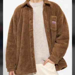 Brun teddyjacka från Acne Studios - Mysig brun teddyjacka från Acne Studios med klassisk krage och bröstficka med broderad logotyp. Jackan är tillverkad i mjuk polyester och har en loose passform. Perfekt för dig som vill ha en trendig och varm look under kyliga dagar. Använt fåtal gånger.  Storlek 44, men väldigt oversized i strl. Skulle säga att den är mer som en L/XL.  Nypris runt 6000:-