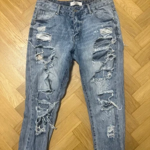 Slitna boyfriend-jeans - Riktigt snygga slitna boyfriend-jeans i tvättad denim. De har flera slitningar både fram och bak. Passformen är lite lösare och kan bäras med uppvik för en ännu mer casual look. Jeansen är i fint skick.Perfekta att matcha med en enkel t-shirt eller hoodie för vardagen, eller klä upp med klackar och topp för en edgy outfit. Storlek är mellan S-M!