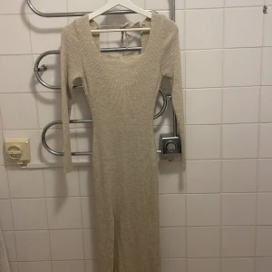 Beige ribbad långklänning med slits - Beige ribbad långklänning med fyrkantig ringning och lång ärm. Klänningen har en snygg slits framtill och knytning i ryggen. 