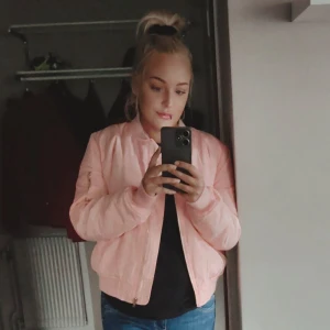 Bomberjacka - Ljusrosa bomberjacka. Ribbade muddar, dragkedja framtill och fickor med tryckknapp i guld/bronze färg