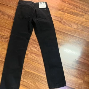 Svarta straight jeans från Karve W28 - Svarta jeans från Karve i rak modell, tillverkade av 100% återvunnen bomull. Klassisk femficksdesign, stone wash finish och diskret Karve-logga på fickan. Perfekta för dig som gillar stilrena och tidlösa jeans.