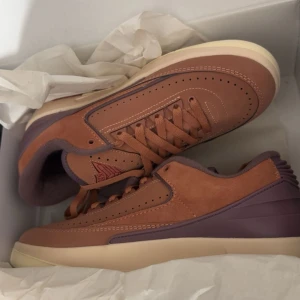 Nike Jordan 2 i brunt och lila - Säljer ett par Nike Jordan 2 sneakers i snyggt brunt och lila med beige sula. Skorna har en mix av mocka och skinn, klassisk snörning och diskreta perforeringar på ovandelen. Perfekta för dig som vill sticka ut med stilrena detaljer och unik färgkombination.