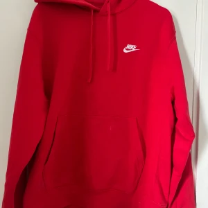 Röd Nike hoodie med logga - Riktigt snygg röd hoodie från Nike med vit broderad logga på bröstet. Klassisk känguruficka framtill, dragsko i huvan och mjukt material som känns skönt mot huden. 