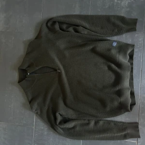 Olivgrön stickad tröja med half zip - Säljer en olivgrön stickad tröja från signal med snygg struktur och ribbade muddar. Tröjan har en praktisk half zip vid halsen och är långärmad. Perfekt för lager-på-lager och chill stil. Använd max 2 gånger. Ny pris 1900kr