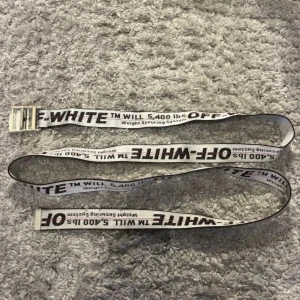 Off-White vitt bälte med text - Säljer ett vitt bälte från Off-White med svart text och metallspänne. Bältet har den ikoniska industriella looken med tryckt logga och detaljerad text längs hela bandet. Perfekt accessoar för att lyfta din streetwear-stil. Finns påse och tags med till bältet