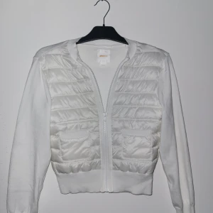 Vit quiltad cardigan jacka Gina Tricot - Supersnygg vit cardigan jacka från Gina Tricot med quiltad framsida och två fickor. Jackan har dragkedja, ribbade muddar och är långärmad. Perfekt för lager-på-lager och ger en fräsch look till jeans eller kjol.