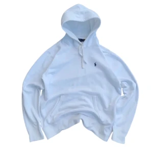 Vit hoodie från Polo Ralph Lauren - Vit hoodie från Polo Ralph Lauren med klassisk huva och snörning. Tröjan har en broderad logga på bröstet och en stor magficka framtill. Tillverkad i mjuk bomull, perfekt för en chill och stilren look. Storlek L kan passa m 