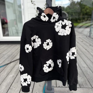 Denim tear hoodie  - Cool svart hoodie med stora vita blommönster över hela tröjan. Oversized passform med huva och känguruficka framtill. Perfekt statement-plagg för dig som vill sticka ut. Mjuk bomullskänsla och långa ärmar.