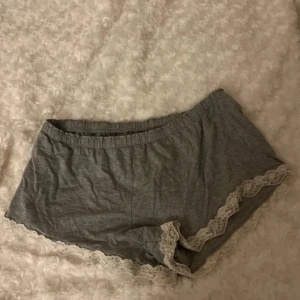 Grå shorts med spets från Lindex - Supermysiga grå shorts från Lindex med elastisk midja och fina vita spetsdetaljer längs kanterna. Perfekta för chill dagar hemma eller som pyjamasshorts. Mjukt bomullsmaterial som känns skönt mot huden.