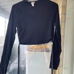 Svart croppad långärmad topp H&M - Svart croppad långärmad topp från H&M med rund halsringning och knytband i sidan. 