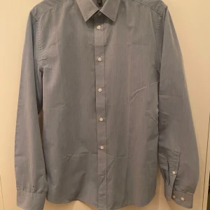 Ljusblå slim fit skjorta från H&M - Snygg ljusblå skjorta från H&M i slim fit-modell. Skjortan har klassisk krage, långa ärmar och knäppning framtill med vita knappar. Tillverkad i bomull och passar perfekt till en clean och stilren look.