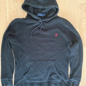 Svart hoodie från Polo Ralph Lauren  - Svart hoodie från Polo Ralph Lauren i storlek XS. Tröjan har huva med snörning, långärmade ärmar. Materialet är bomull med en grovstickad struktur och den ikoniska röda Polo-loggan broderad på bröstet. Skick 9/10 För fler frågor kom pm! /Neo