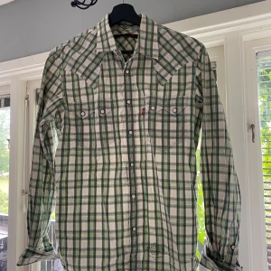 Rutig skjorta från Levi's  - rutig skjorta från Levi's i vitt, grönt, gult och brunt. Skjortan har långa ärmar, tryckknappar och två bröstfickor med lock. Storlek M men funkar M/S, obs säljs på fler sidor