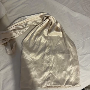 Champagnefärgad satintopp med knyt - Säljer en champagnefärgad satintopp med breda knytband som kan stylas på olika sätt. Toppen har en glansig finish och smockad rygg för extra komfort och passform. Perfekt för dig som vill ha en trendig och elegant look.