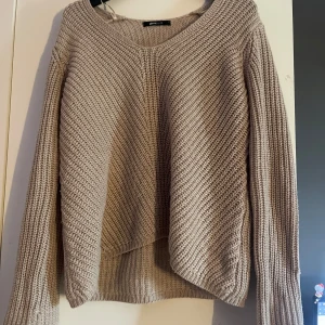 Beige stickad tröja från Gina Tricot - Mysig beige stickad tröja från Gina Tricot med v-ringad hals och lång ärm. Tröjan har en lite loose passform och ribbade muddar vid ärmslut och nederkant. Perfekt för lager-på-lager under kyliga dagar.