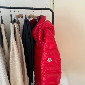 Röd Moncler dunjacka strl 4 - Säljer en riktigt fet röd dunjacka från Moncler. Jackan har glansig finish, klassisk pufferstil och ikonisk Moncler-logga på ärmen. Fodrad insida i brunt och dragkedja framtill. Perfekt för kalla dagar när du vill sticka ut.