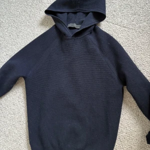 Mörkblå stickad hoodie från MNG - Mysig mörkblå stickad hoodie från MNG i storlek S. Tröjan har en klassisk huva och är långärmad, perfekt för kyliga dagar. Enkel och stilren design som funkar till många olika outfits.