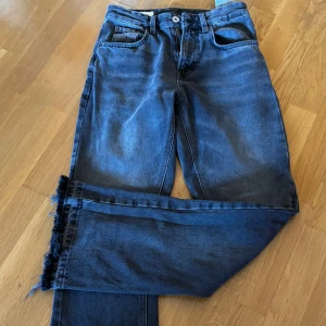 Mörkgråa  jeas från Zara flared  - Snygga mörkblå jeans från Zara med raka ben och trendig rå, fransad kant nertill. Klassisk femficksmodell i kraftigt jeanstyg som ger en cool och avslappnad vibe. Perfekta för dig som gillar en stilren men edgy look.