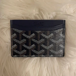 Goy4rd korthållare i mörkblått mönster - Säljer en snygg korthållare från Goy4rd i mörkblått med deras ikoniska grafiska mönster i vitt och brunt. Korthållaren är tunn och smidig, perfekt för kort och lite cash. Tillverkad i skinn och levereras med originalask och dustbag. Riktigt stilren accessoar för dig som gillar lyxiga detaljer.