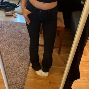 Svarta bootcut jeans med låg midja  - Säljer ett par svarta jeans med bootcut-modell och låg midja. Jeansen har klassisk femficksdesign och är i stretchigt denimtyg som sitter snyggt över höfterna och låren. Perfekta för dig som gillar en tidlös och clean look.