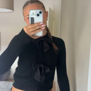 Svart kofta med rosetter från H&M - Supersöt svart kofta från H&M med två stora tygrosetter framtill. Koftan är stickad, har lång ärm och en klassisk passform. Perfekt för dig som gillar detaljer och vill ha en mysig men ändå stylish look. Koftan stängs även med knappar. För flera bilder skriv 💕