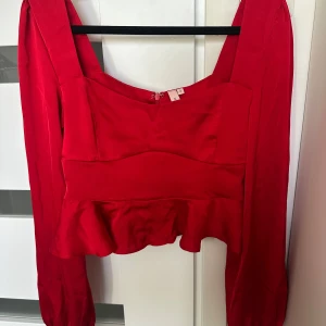 Röd volangtopp från Nelly - Säljer en snygg röd topp från Nelly med långa ärmar och volang nertill. Toppen har fyrkantig urringning och dragkedja i ryggen. Perfekt för dig som vill sticka ut med en färgstark look.