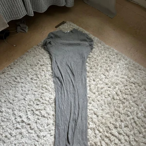 Grå ribbad långklänning - Säljer en grå långklänning med ribbad struktur och korta ärmar. Klänningen har en enkel, rak passform och rund halsringning. Perfekt för dig som gillar stilrena och bekväma plagg.