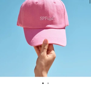 Rosa keps med broderad text SPFUN! Ifrån värde 249kr GlowiD  - Snygg rosa keps med vit broderad text 'SPFun!' framtill. Klassisk böjd skärm och justerbar passform. Tillverkad i bomull för en bekväm känsla och perfekt för soliga dagar. Värde 249kr GlowiD 