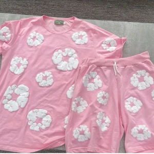Rosa t-shirt med vita blommor - Säljer en rosa t-shirt från Cactus Jack med stora vita blommiga mönster över hela tröjan. T-shirten har rund halsringning och är kortärmad. Perfekt för dig som gillar färg och unika prints.