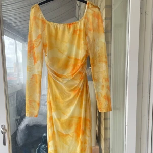 Gul och orange långklänning från SHEIN - Långklänning från SHEIN i storlek M med ett unikt mönster i gula och orange toner. Klänningen har långa ärmar, rundad halsringning och lätt drapering framtill. 