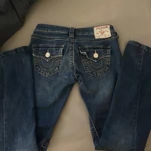 True Religion blå jeans - Säljer ett par blå jeans från True Religion med ikoniska kontrastsömmar och snygga fickdetaljer med knappar bak. Jeansen har klassisk femficksdesign och tydlig logga på bakfickan. Perfekta för dig som gillar streetwear och vill sticka ut. dom är lite slitna där nere som knappy syns❤️ storlek 24