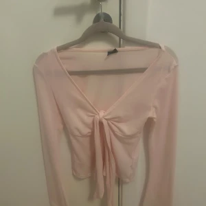 Ljusrosa omlottopp från Gina Tricot - Säljer en ljusrosa omlottopp från Gina Tricot i storlek XS. Toppen har lång ärm, v-ringning och snygg knytning framtill. Materialet är tunt och mjukt, perfekt för vår och sommar. Enkel att styla med jeans eller kjol för en söt look. Passar xxs, xs och s!