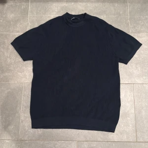 Mörkblå ribbad tröja från Zara - Snygg mörkblå ribbad tröja från Zara med korta ärmar och hög krage. Tröjan har en clean och stilren look, perfekt för dig som gillar minimalistisk stil. Materialet är mjukt och känns skönt mot huden. Passar dig som vill ha en enkel men trendig topp.