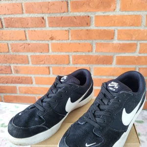 Nike SB Force 58 svarta sneakers - Svarta Nike SB Force 58 sneakers med vit sula och vit swoosh på sidorna. Skorna har snörning och är tillverkade i mocka och textil, vilket ger en skön och slitstark känsla. Perfekta för skate eller streetstyle.